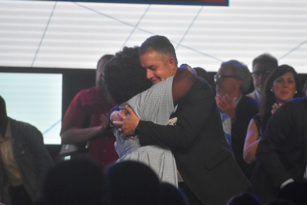 A woman in a blue dress hugs a man in a suit.