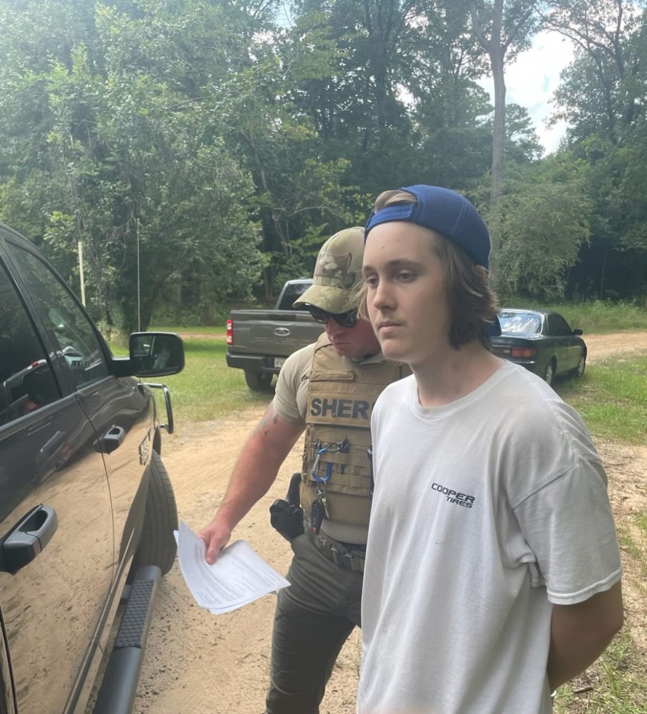 A man in a white shirt and backwards hat on. An officer with his uniform on is standing next to him.