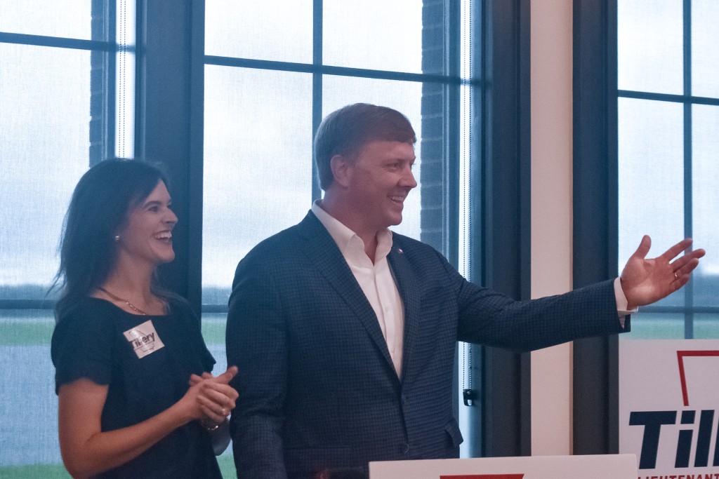 A man in a suit standing at a podium. A woman in a dress is standing next to him. Both are smiling.