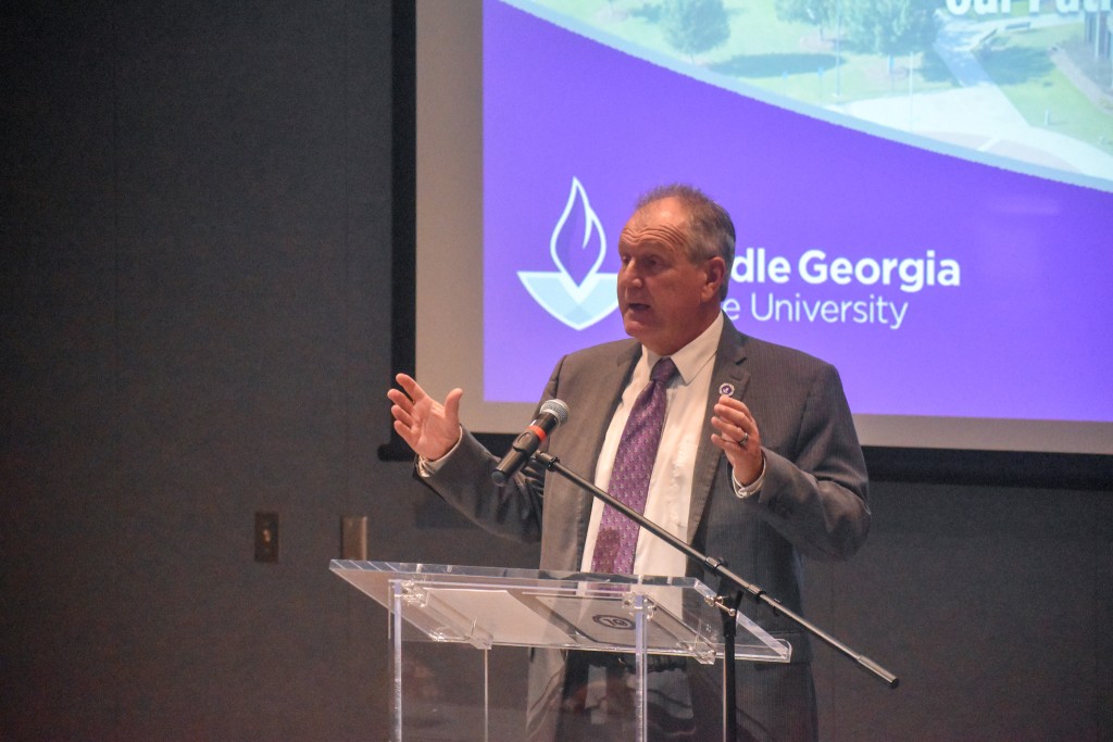 A man in a suit standing behind a podium speaking to an audience.
