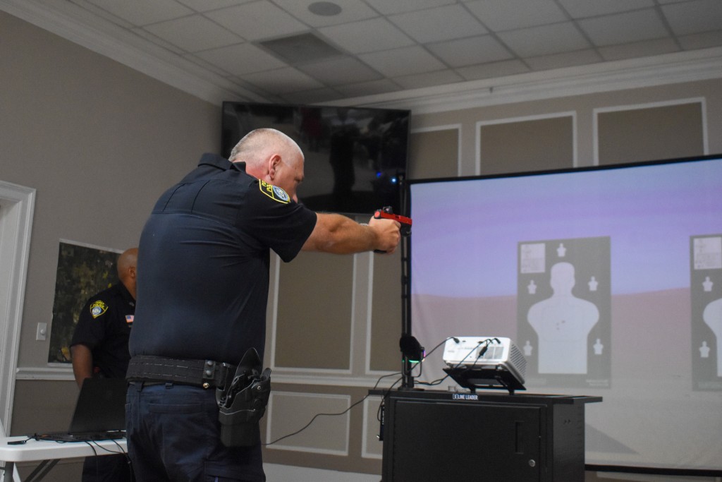 A man in a police uniform aiming a gun simulator at a screen. 