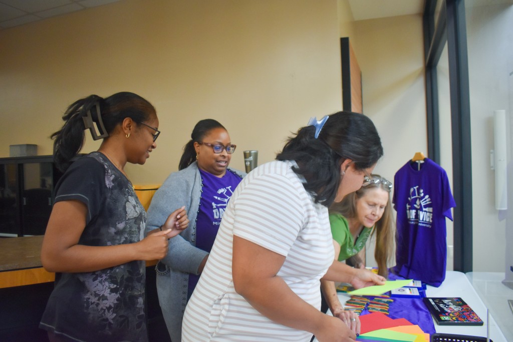 Four women standing over a table which has colored paper and markers.