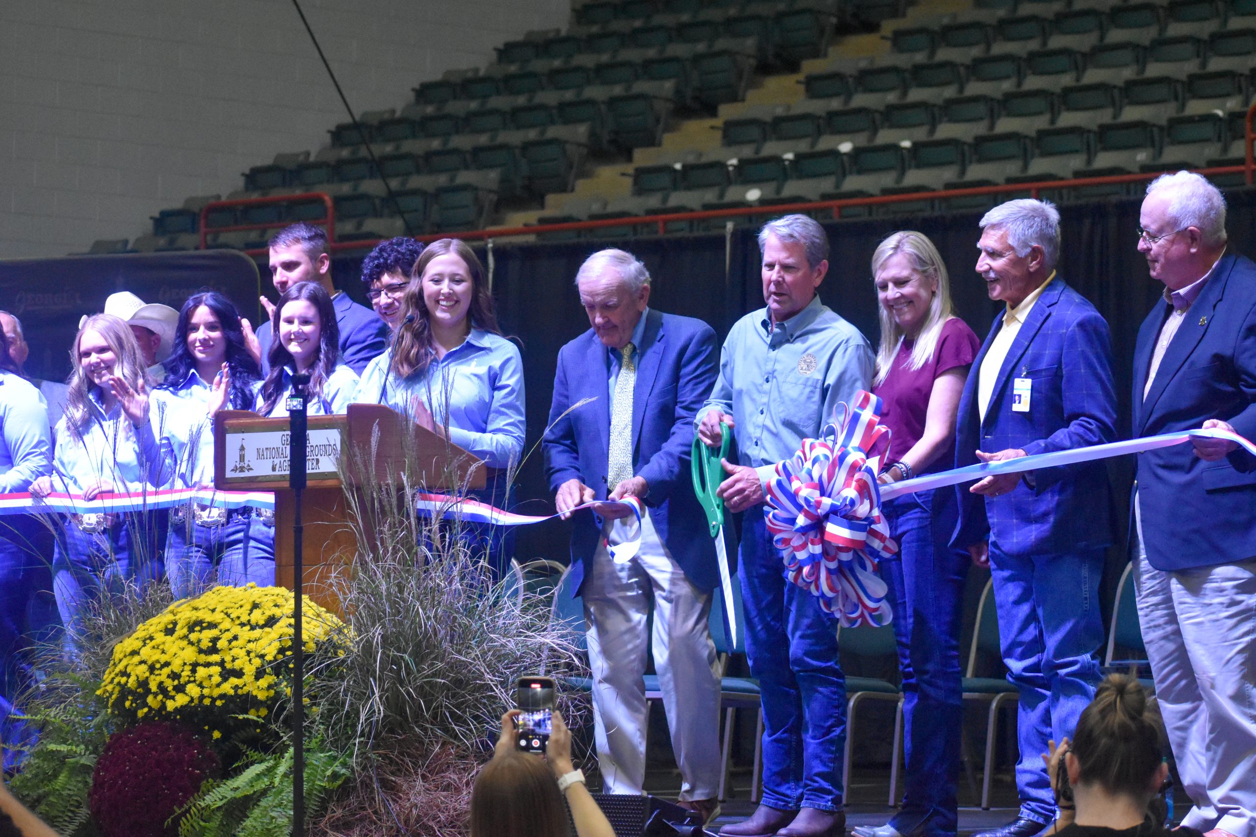 group of people standing on stage with a ribbon that had been cut
