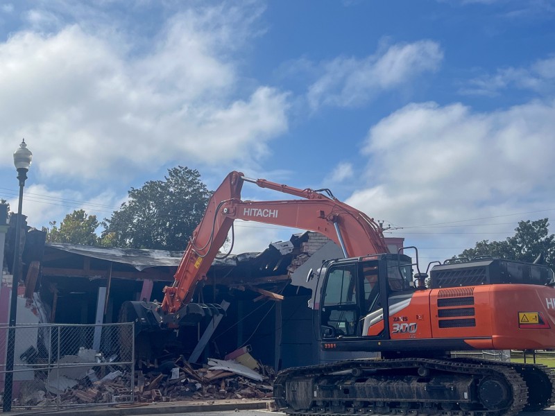 An orange excavator in front of a rumbles of a building.