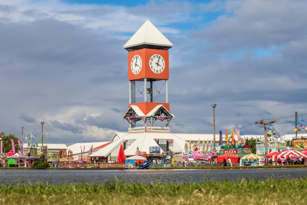 An orange and white clock tower. Below there are colorful tents.