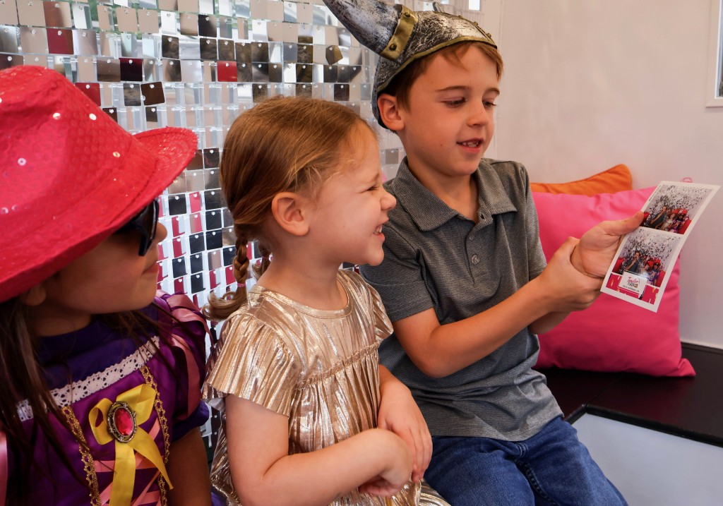 Three children: Two girls and one boy smiling. They are looking at a photo being held by the boy. 