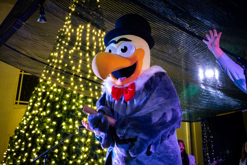 Bob the Buzzard mascot on a stage. Behind him is a Christmas tree. It is night time.