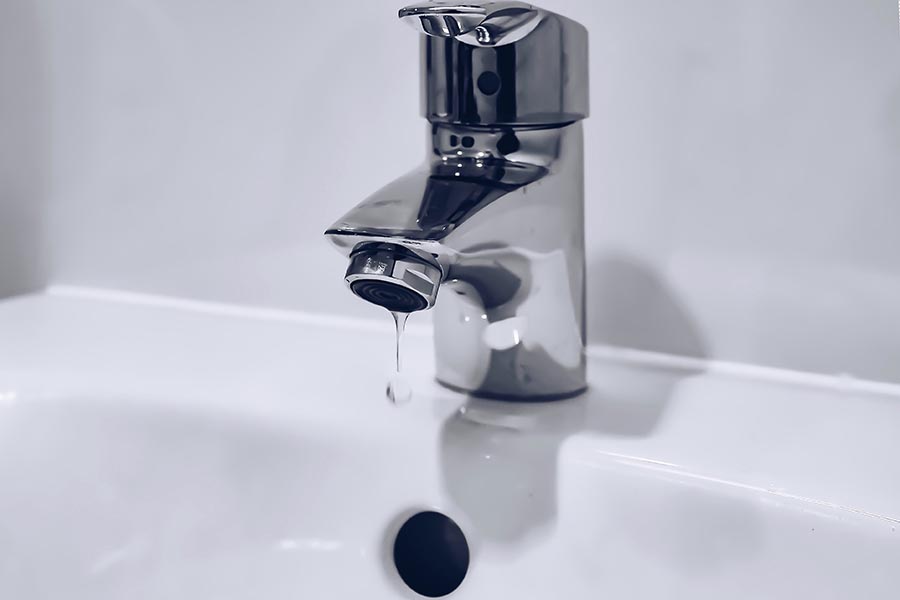 A white sink with a silver water faucet. Water is dripping out of the faucet.