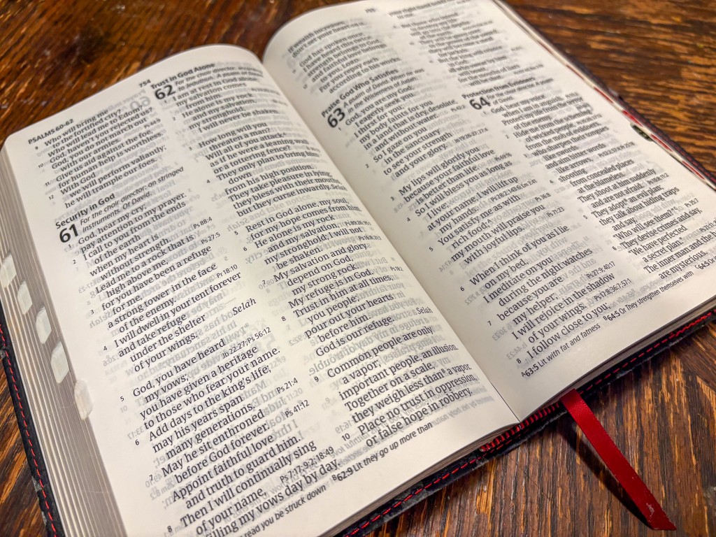 Photo of an open book on a wooden table. The book is the Bible.