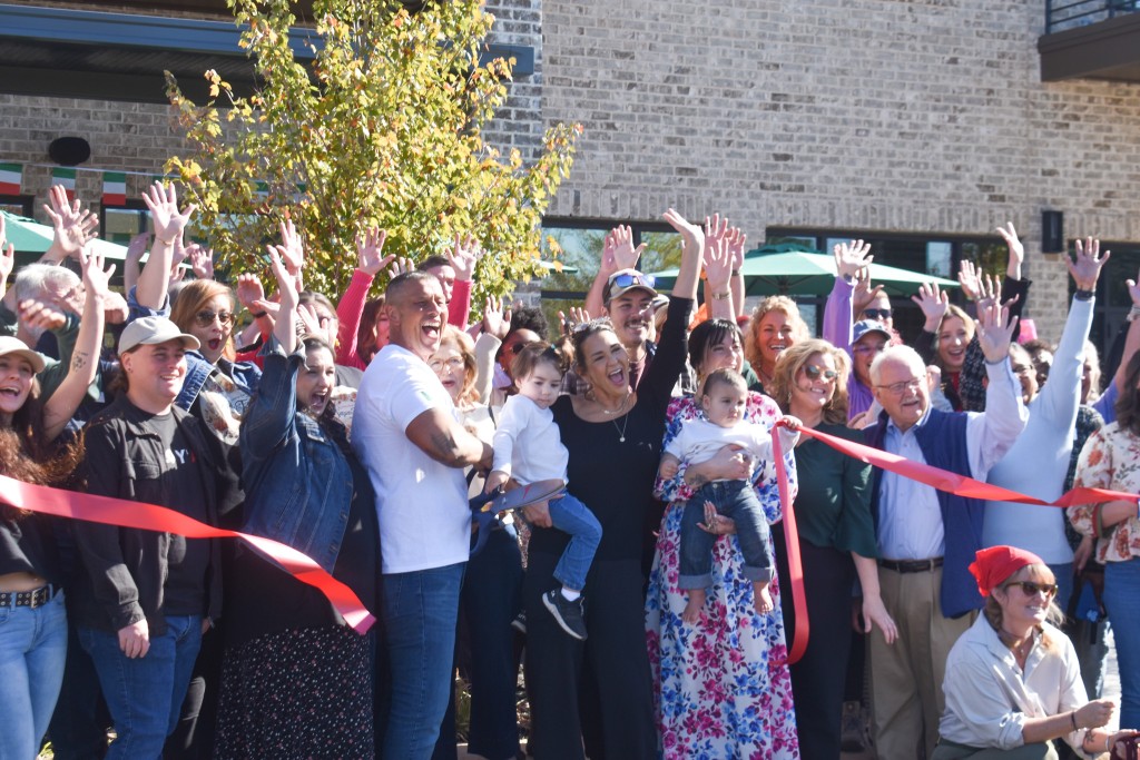 A group of people with their hands in the air smiling. A red ribbon is in front of them. 