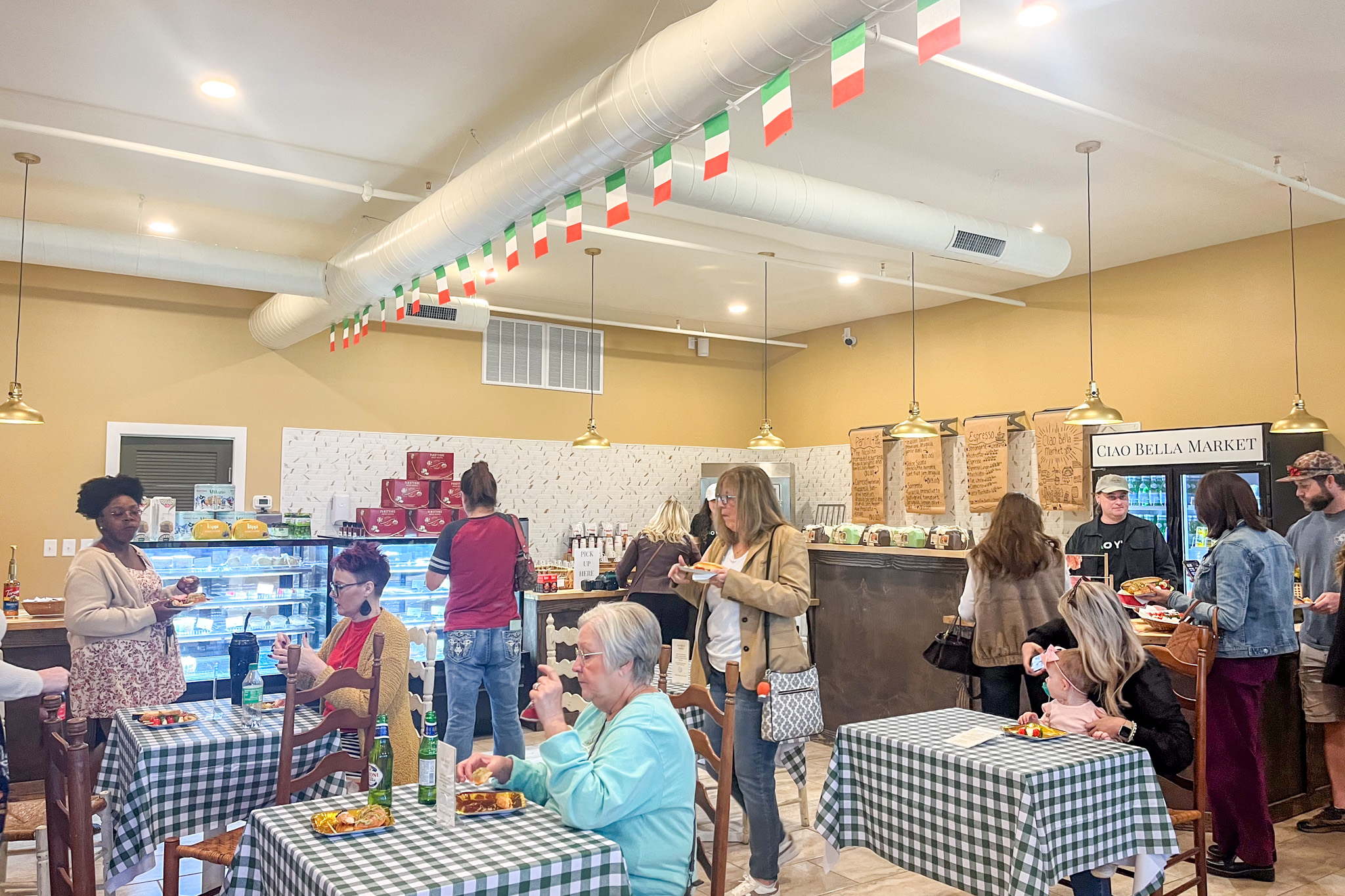 A room with tables, and people sitting down. Little Italian flags are hanging on the ceiling.