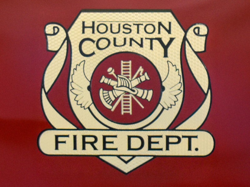 The Houston County Fire Department. It is gold with black words. There is a red background