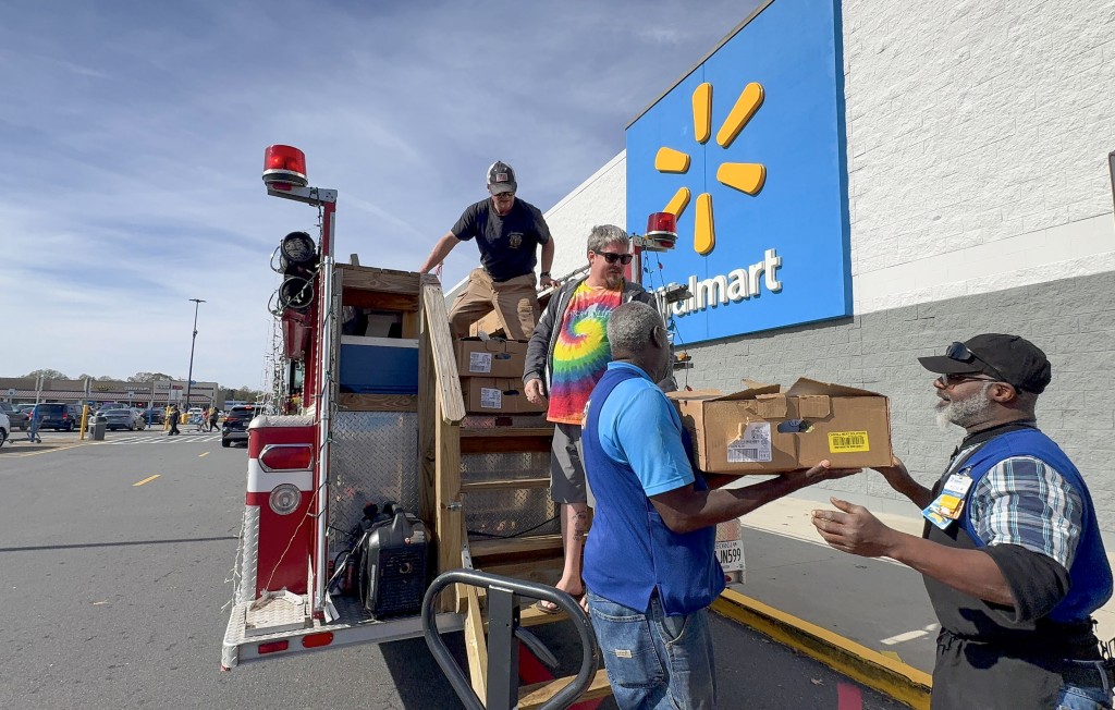 Three men carrying boxes. One of them is on a fire truck.