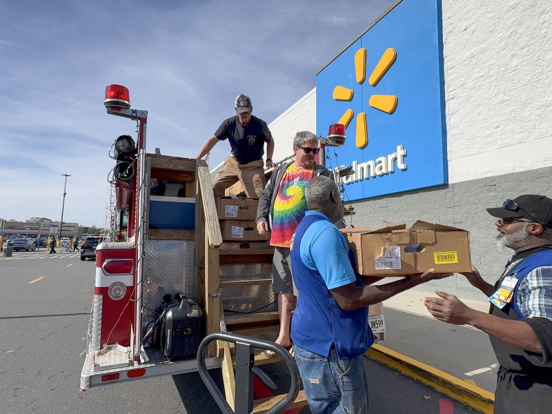Three men carrying boxes. One of them is on a fire truck.