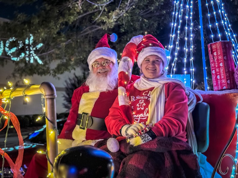 On the left, an older man dressed as Santa Claus sits next to an older woman also wearing a red Santa Claus hat.