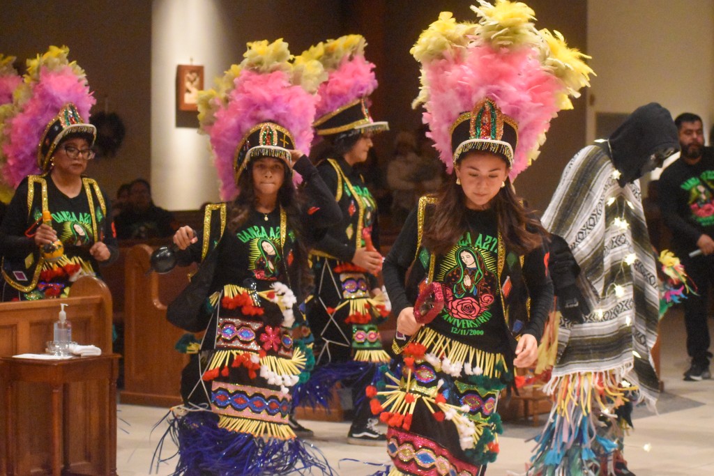 Two girls dancing. Both are wearing feathered hats and traditional Aztec clothing. 