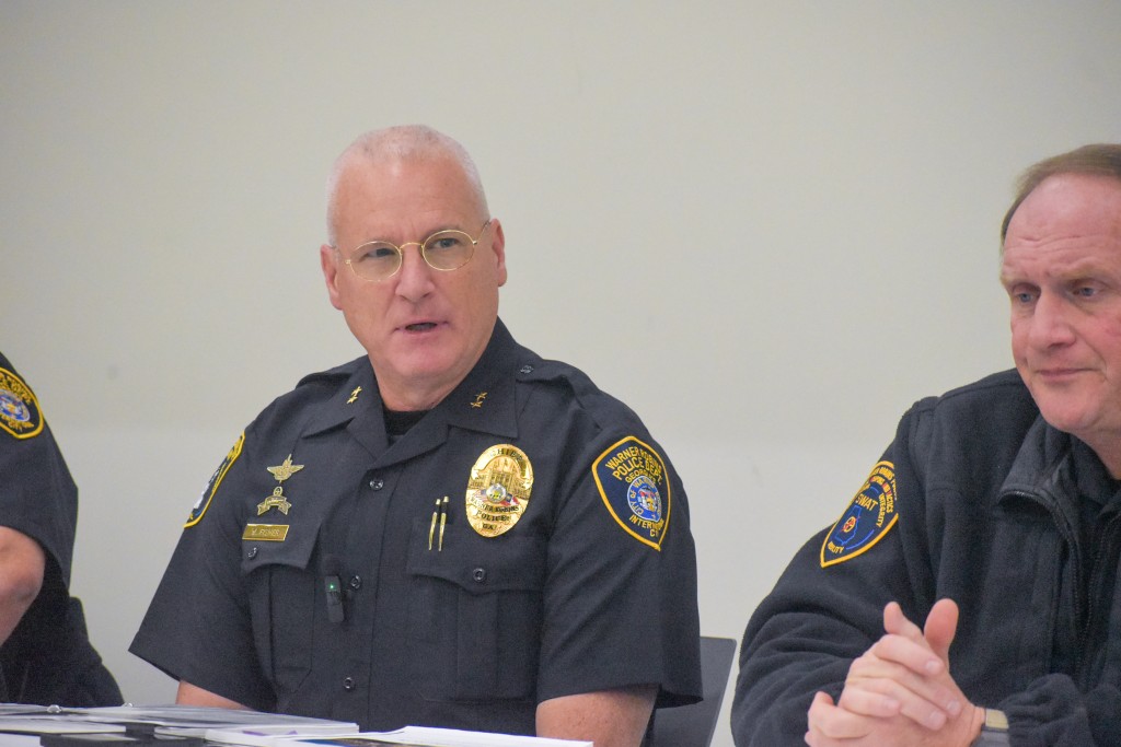 Two men in a black police uniform sitting at a table. One of the men is sitting in the middle talking. 