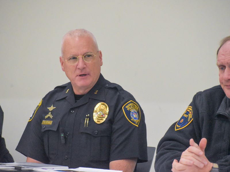 Two men in a black police uniform sitting at a table. One of the men is sitting in the middle talking.
