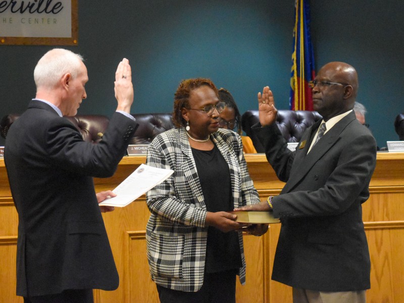 Two men standing across from each other raising their right hand. One of the men has their left hand on the Bible. A woman is standing between them holding the Bible.