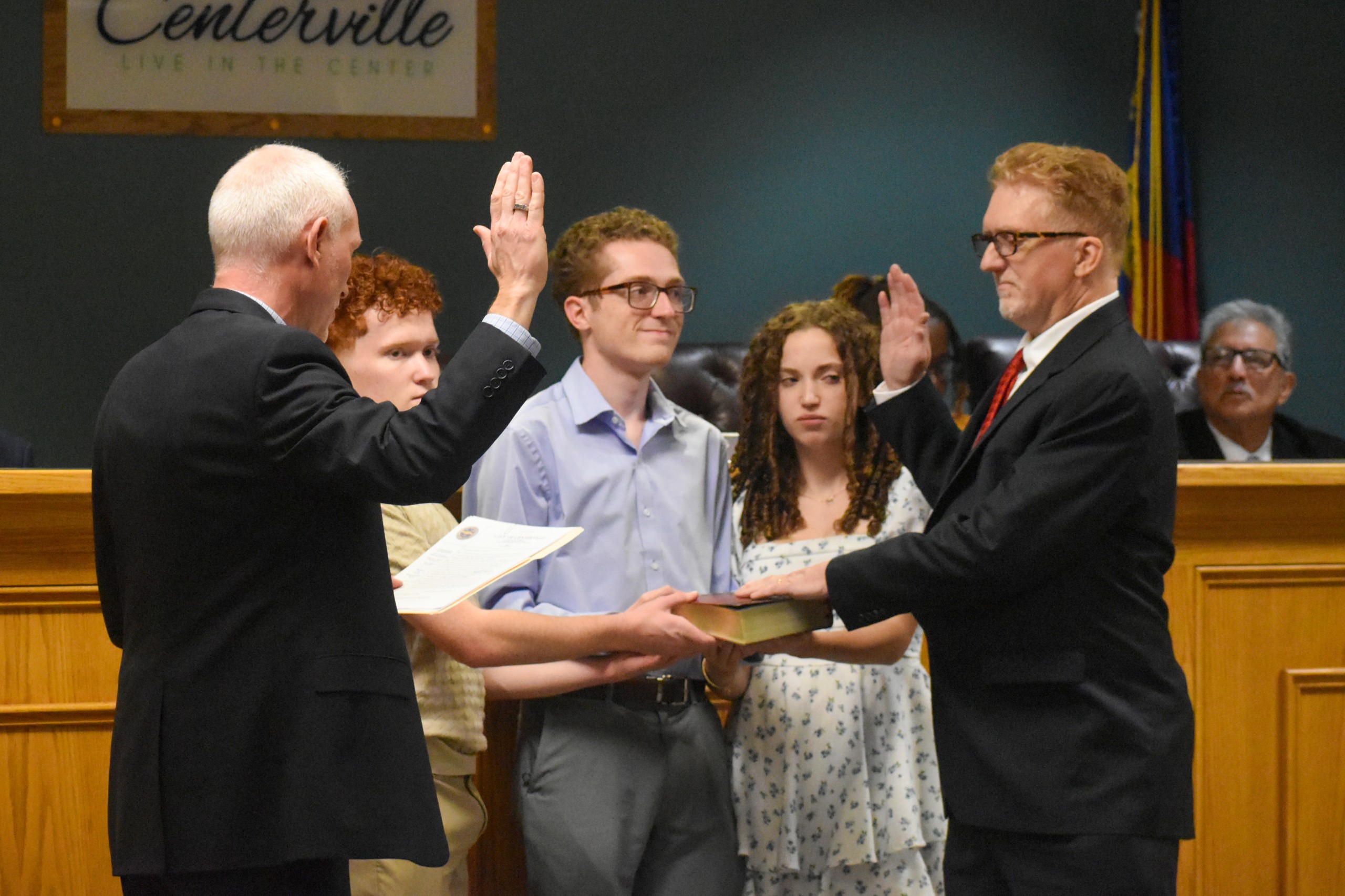 Two men standing across from each other raising their right hand. One of the men has their left hand on the Bible. Two boys and a girl are standing between them, holding the Bible.