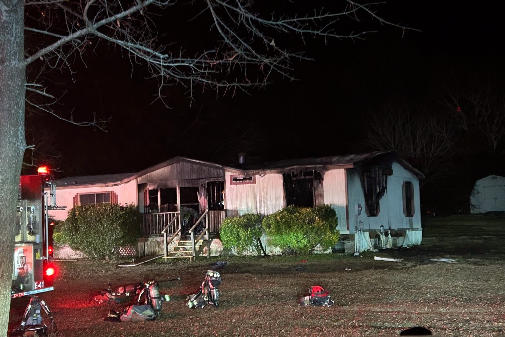 A home with fire damage. There is a fire truck with sirens in front of the home. The photo was taken at night. 