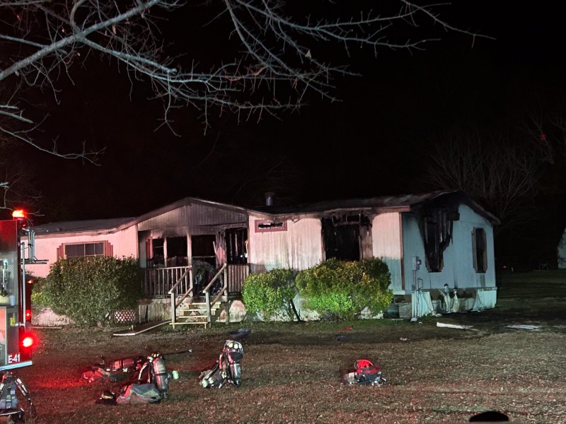 A home with fire damage. There is a fire truck with sirens in front of the home. The photo was taken at night.