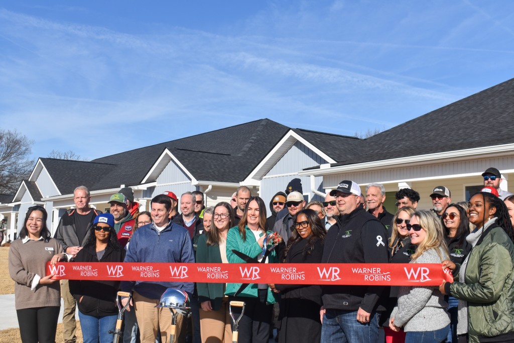 A group of people smiling. There is a red ribbon in front of them.