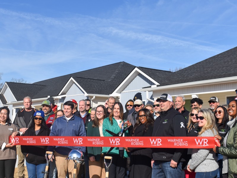 A group of people smiling. There is a red ribbon in front of them.