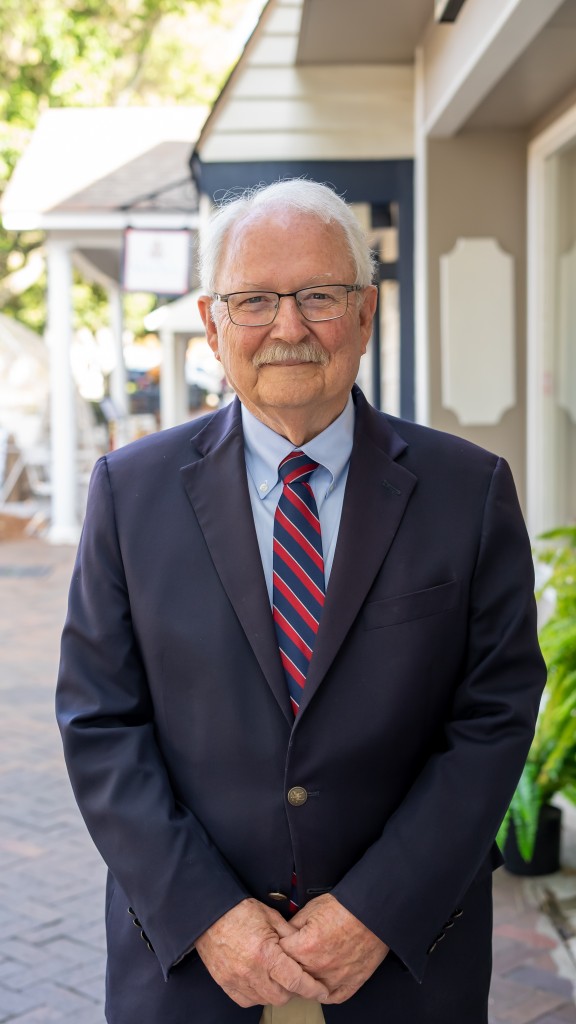 An older man with a suit and red and blue tie. He is smiling.