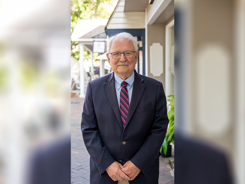 An older man with a suit and red and blue tie. He is smiling.