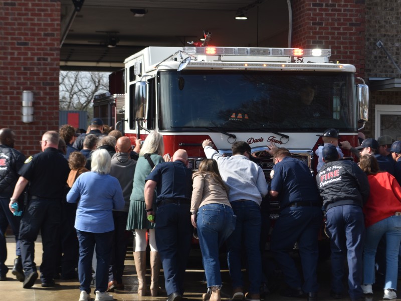 group of people pushing firetruck into the station