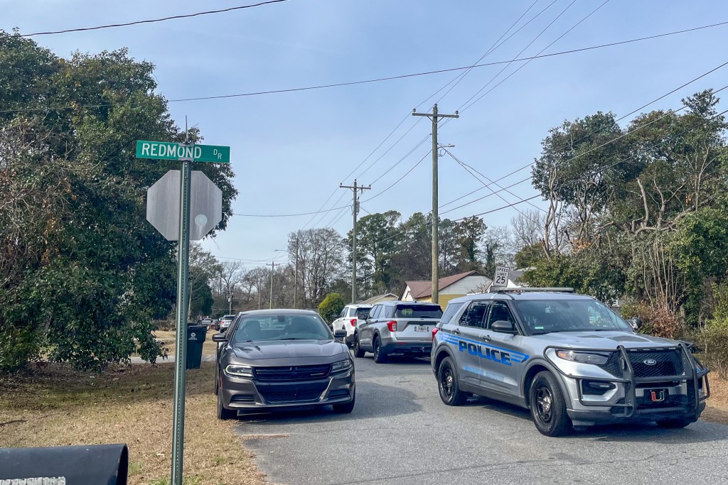 A silver police vehicle on the road. There is a street sign on the left. 
