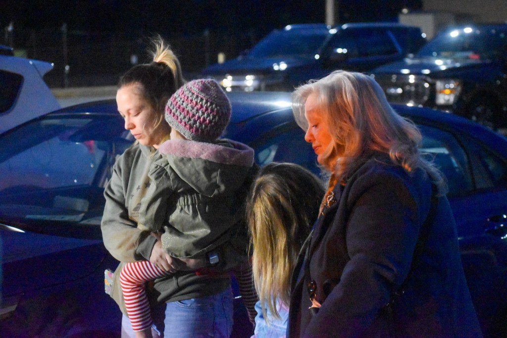 A woman with her eyes closed holding a little girl. Next to her is another little girl and an older women, also with their eyes closed.