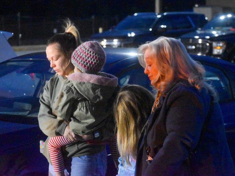A woman with her eyes closed holding a little girl. Next to her is another little girl and an older women, also with their eyes closed.