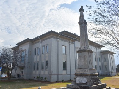 A tall gray statue standing in front of a large gray building. It is a sunny day.