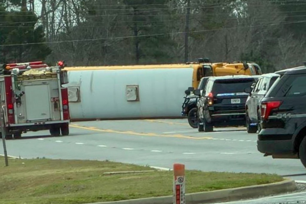 Black vehicles and a fire truck in front of a yellow school bus. It is in the middle of a street. 