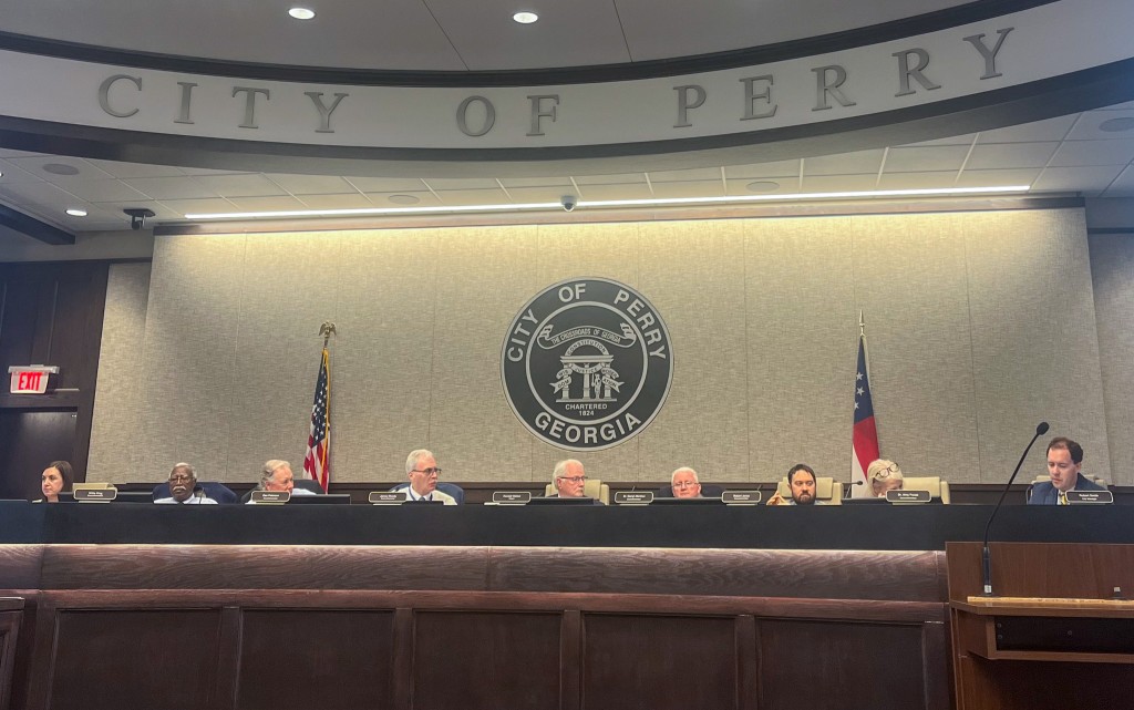 A group of people sitting behind a large brown desk. They are in the council chambers.