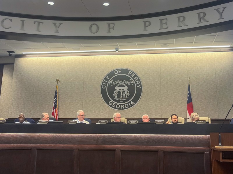 A group of people sitting behind a large brown desk. They are in the council chambers.