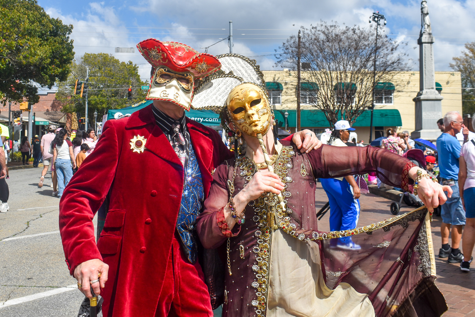 A man, standing on the left, and woman, standing on the right, dressed in colorful clothing and masks. The woman was wearing a gold mask and the man was wearing a white and red mask.