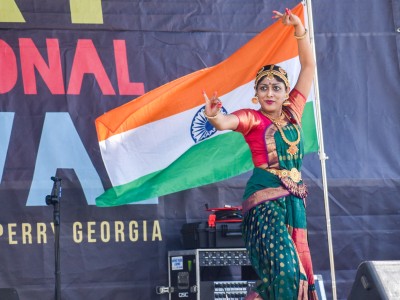 A woman in traditional Indian clothing dancing. Behind her is the Indian flag which is orange, white and green.
