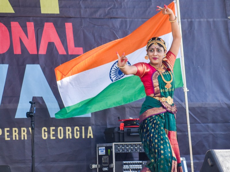 A woman in traditional Indian clothing dancing. Behind her is the Indian flag which is orange, white and green.