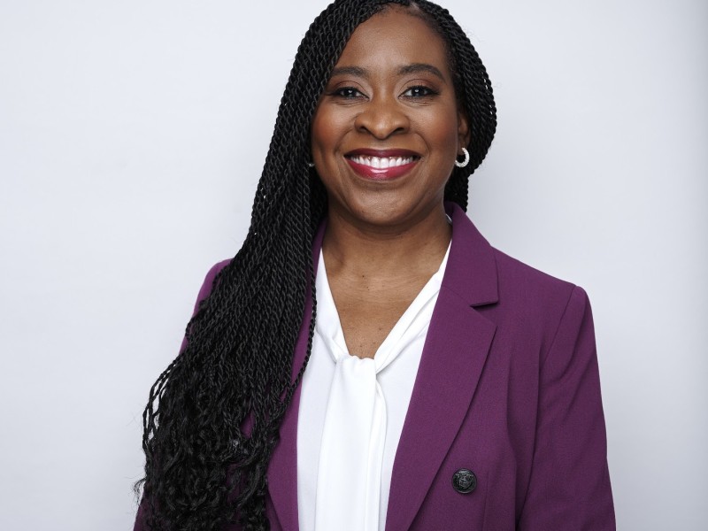 A woman in a purple suit and white shirt smiling.