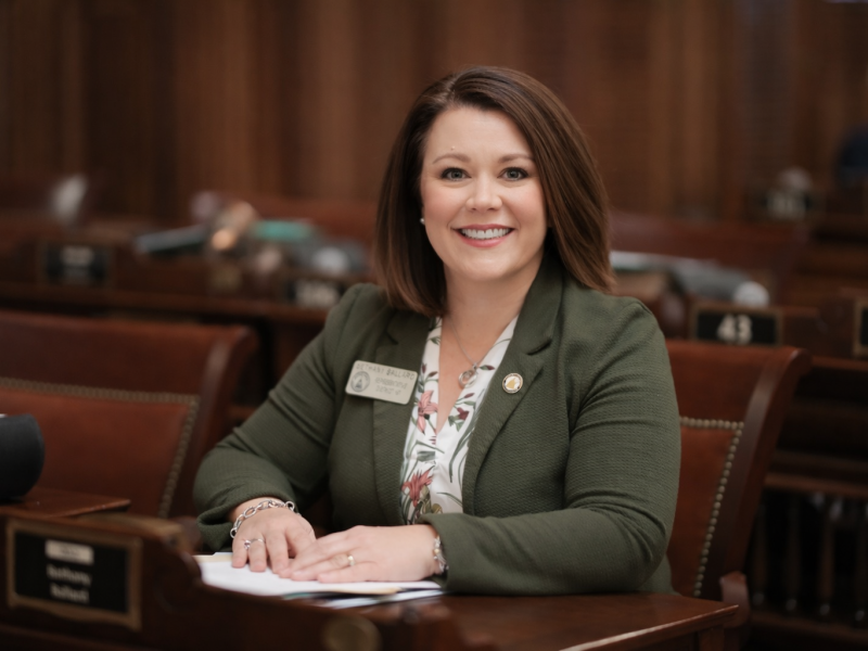 A women sitting down behind a desk. She is smiling.