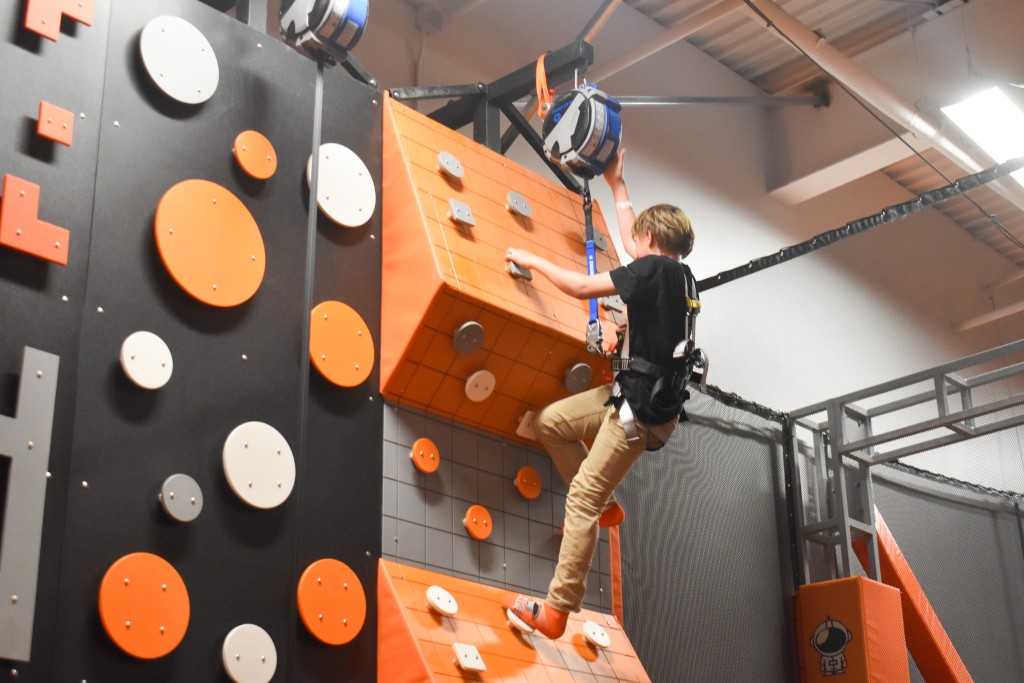 A boy climbing on a rock climb wall. The wall is orange, white and black. 