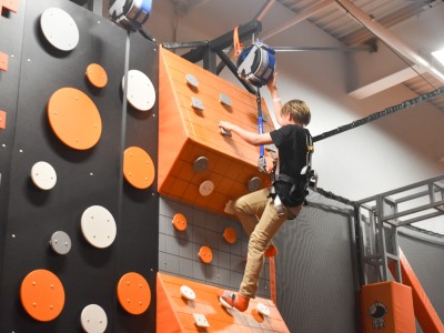 A boy climbing on a rock climb wall. The wall is orange, white and black.