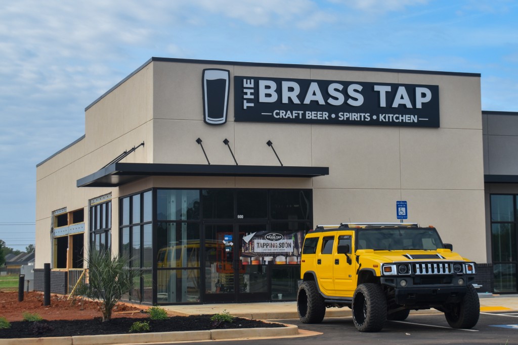 A building with a sign that says,"Brass Tap" in silver lettering. There is a yellow car in front of the building. 