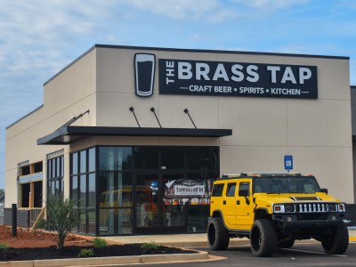 A building with a sign that says,"Brass Tap" in silver lettering. There is a yellow car in front of the building.