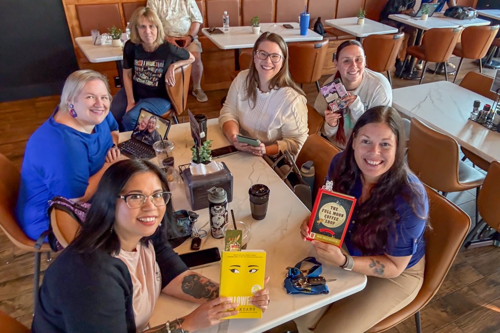 A group of women sitting at a table holding a book. They are all smiling.