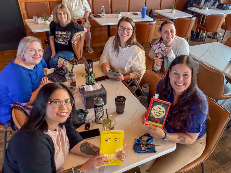 A group of women sitting at a table holding a book. They are all smiling.