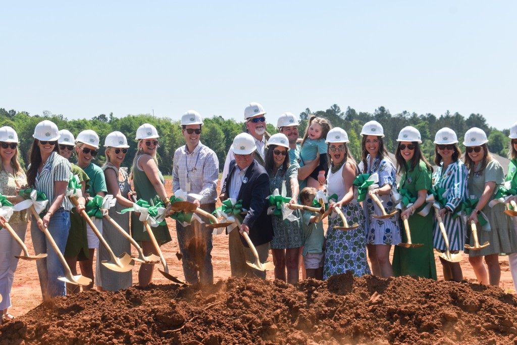 A group of people holding shovels. They are standing over dirt and smiling. 